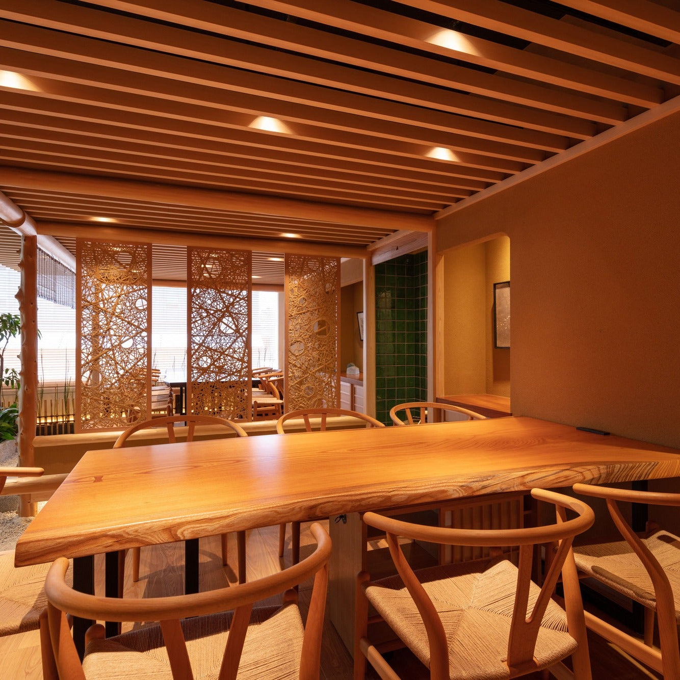 A solid-timber meeting table faces woven lattice screens and a courtyard of horsetail and stone in the Japanese office.