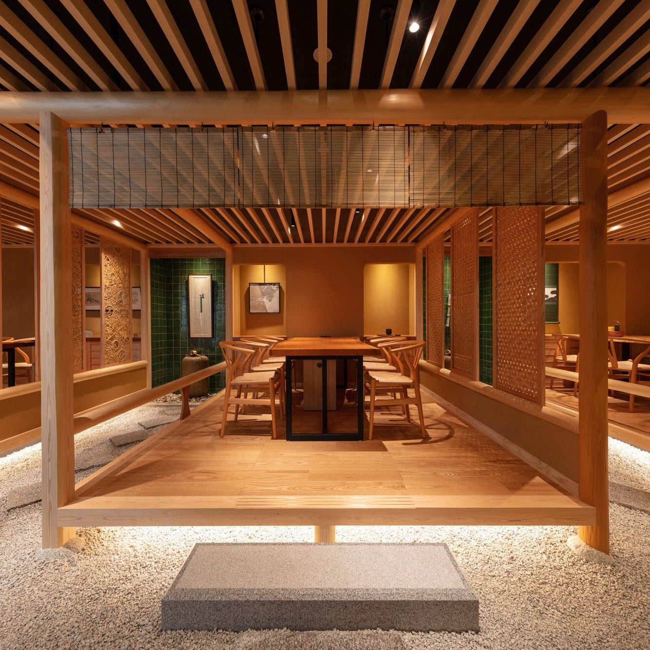A long meeting table on a timber platform set within raked gravel, screened by woven panels, a Japanese office room.
