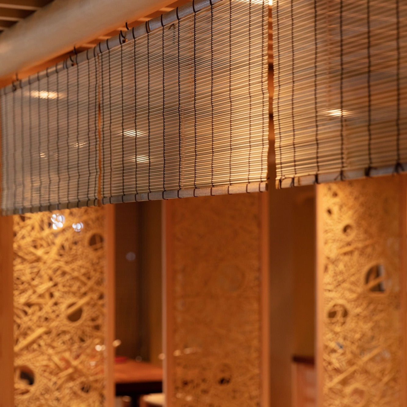Close detail of a bamboo reed blind hung above open woven-twig lattice panels.