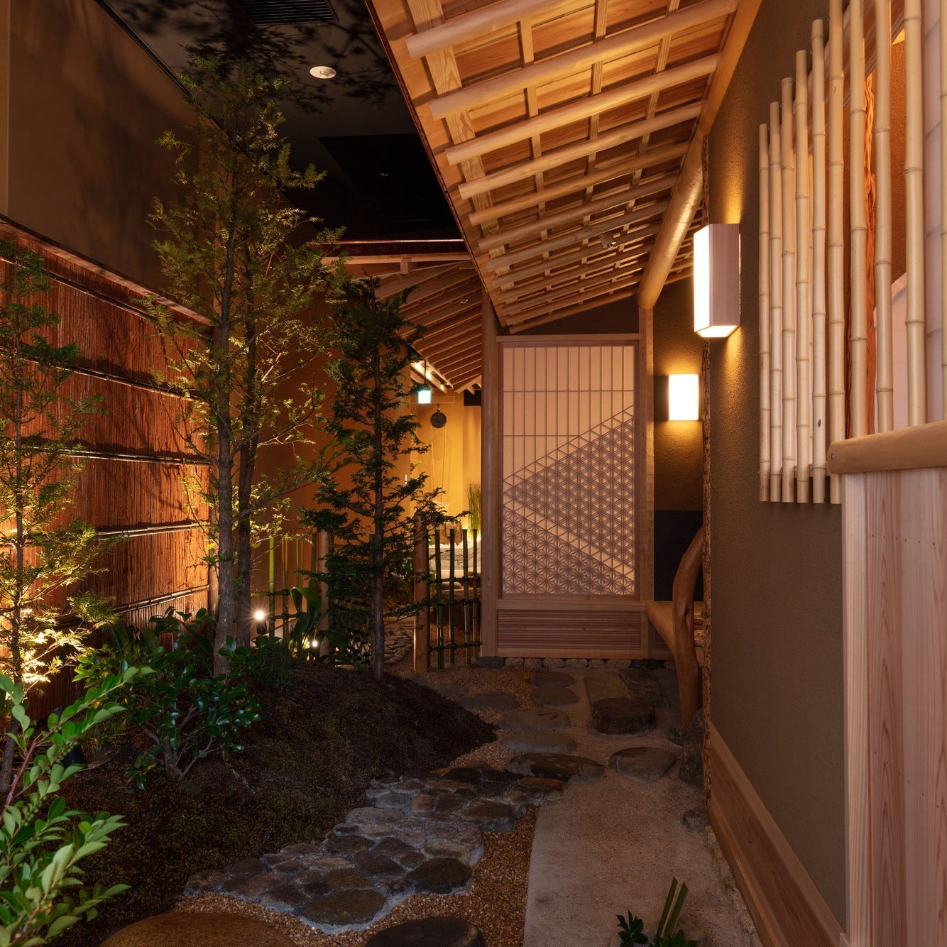 Stepping stones lead along a softly lit garden path at night, a quiet passage of Japanese architecture.