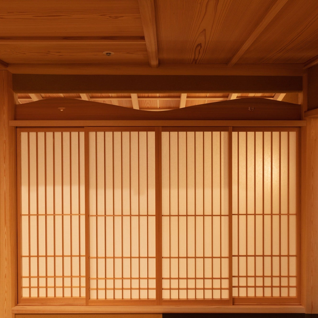 Quatre shoji sous une imposte découpée en vagues, le tout sous un plafond de planches