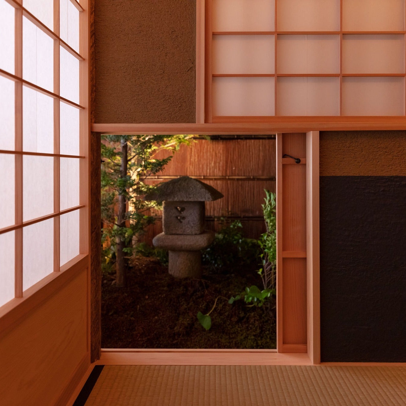 A low window frames a stone lantern in a small inner courtyard garden, seen from the tatami edge.
