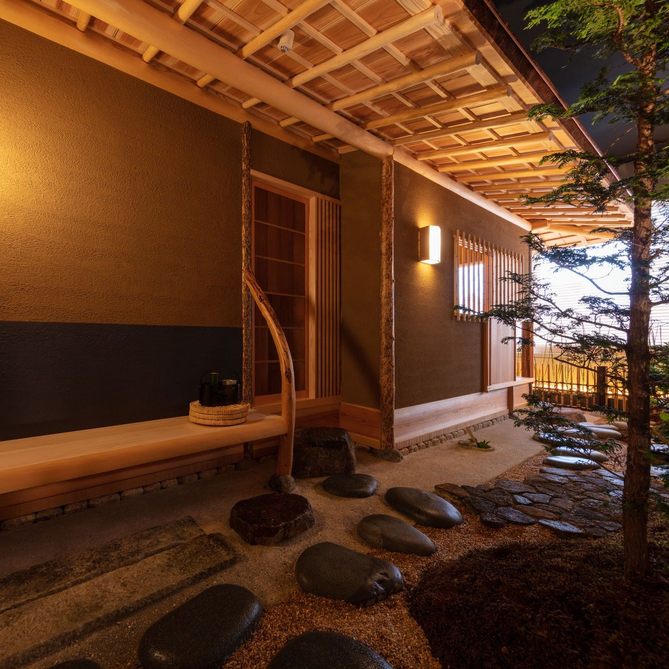 A wooden waiting bench beside a stepping-stone path, set for guests arriving at the chashitsu.