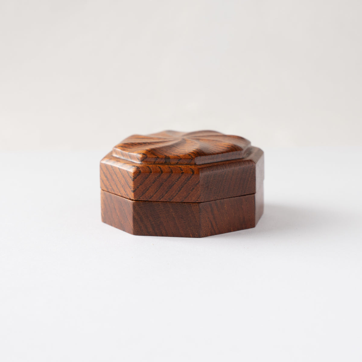Eye-level side profile of the closed octagonal Keyaki wood KOGO incense container by Osamu Oyama, highlighting the carved lid elevation.