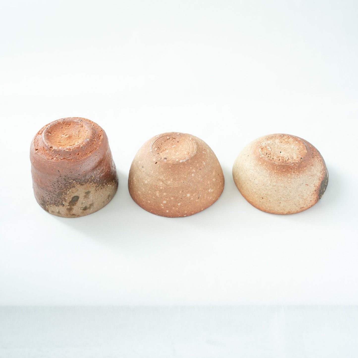 Inverted view of the three Shigaraki GUINOMI, showing the simple unglazed bases and the diverse textures of the fired mountain clay.