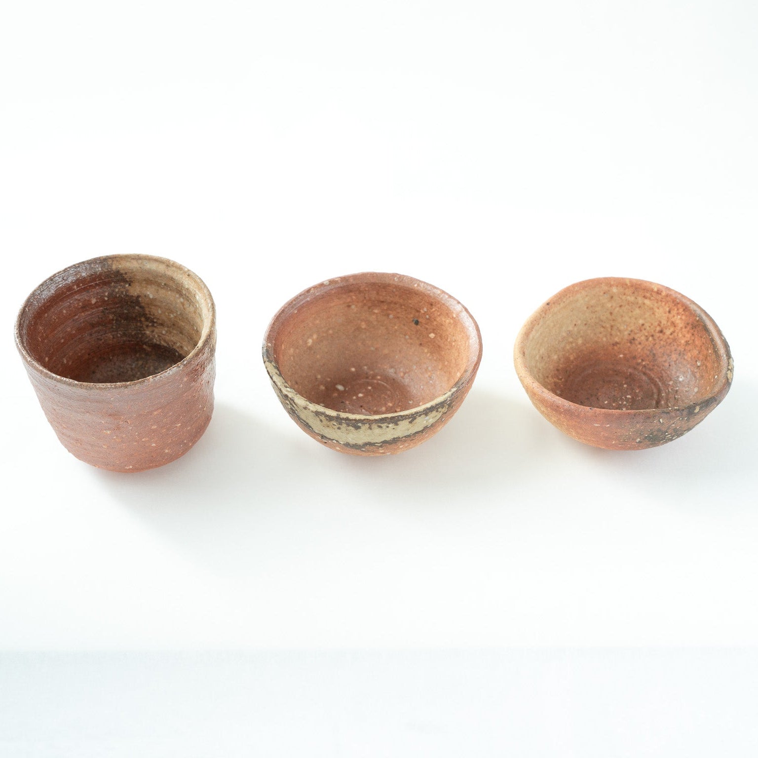 Top-down angled view looking into the interiors of the three Shigaraki cups, revealing variations in depth, wheel marks, and inner glaze pooling.