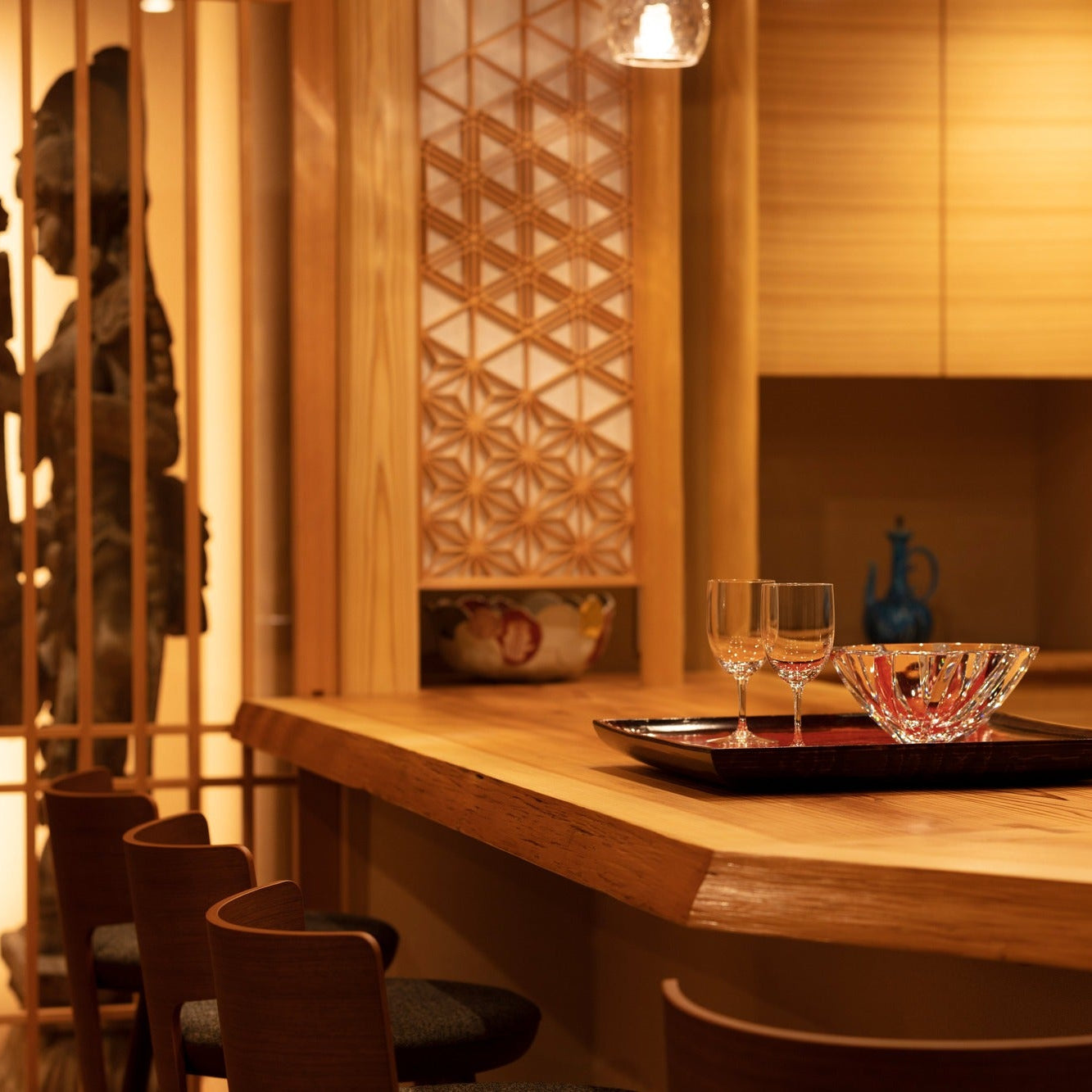 Close view of cut-glass ware on a lacquer tray atop a live-edge counter, beside a kumiko asanoha lattice panel.