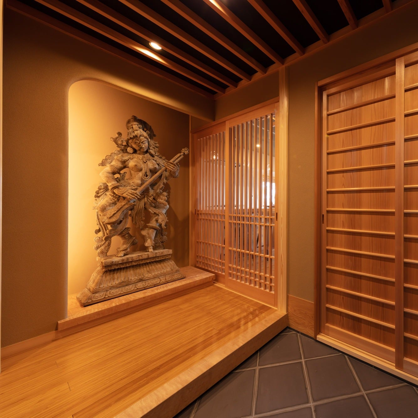 Entrance hall with a hand-carved deity on a single horse-chestnut plank shelf, cedar sliding doors and a tiled floor.