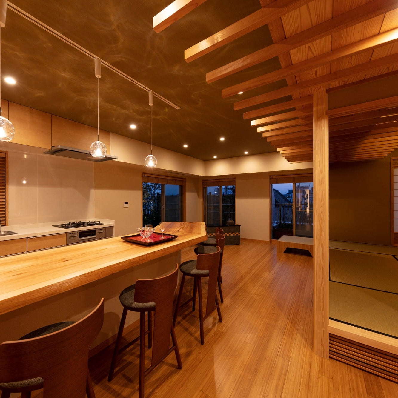Long kitchen counter with glass pendant lights at dusk, a tatami room with shoji screens visible to one side.