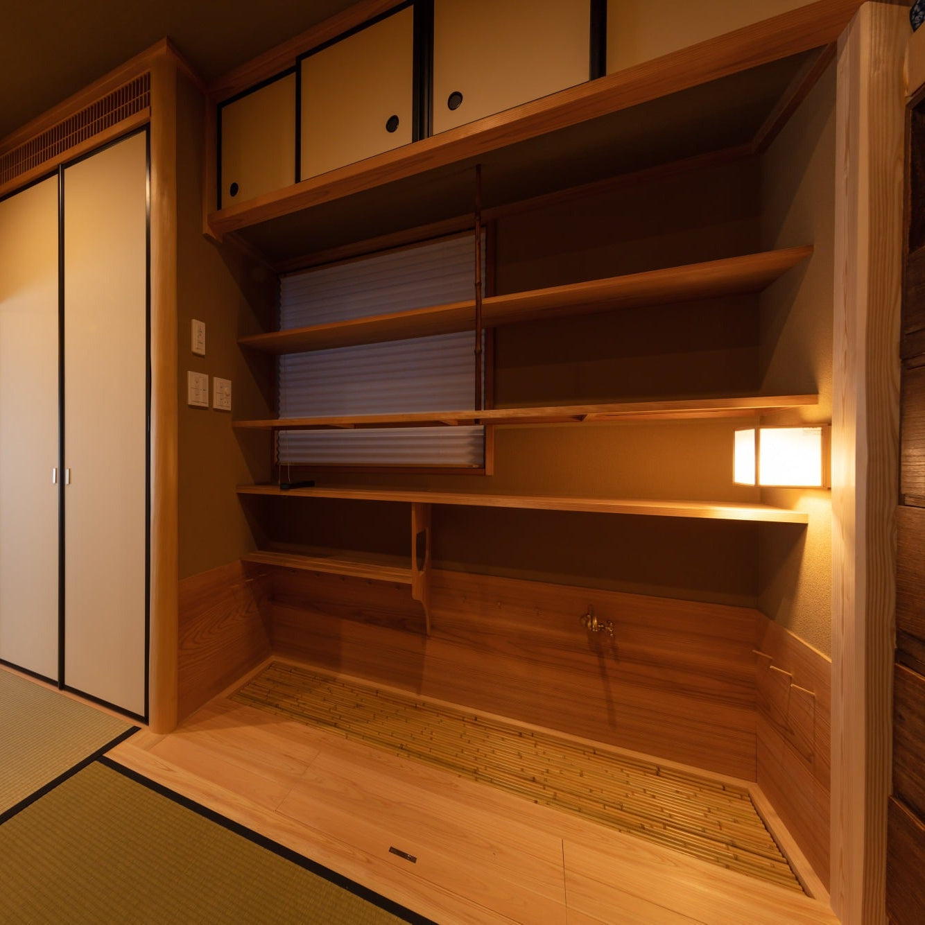 Mizuya preparation room with cedar shelving and a bamboo-slat base, opening toward the tatami hall.