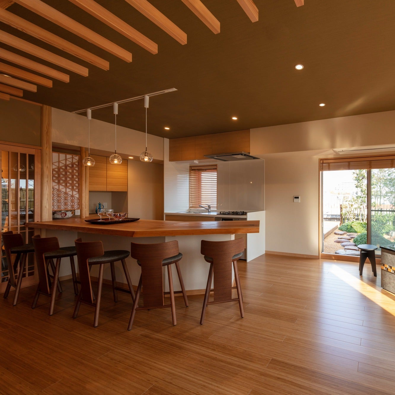 Daytime salon counter looking onto a rooftop garden, with a black-topped hearth and an iron kettle beside floor-to-ceiling windows.