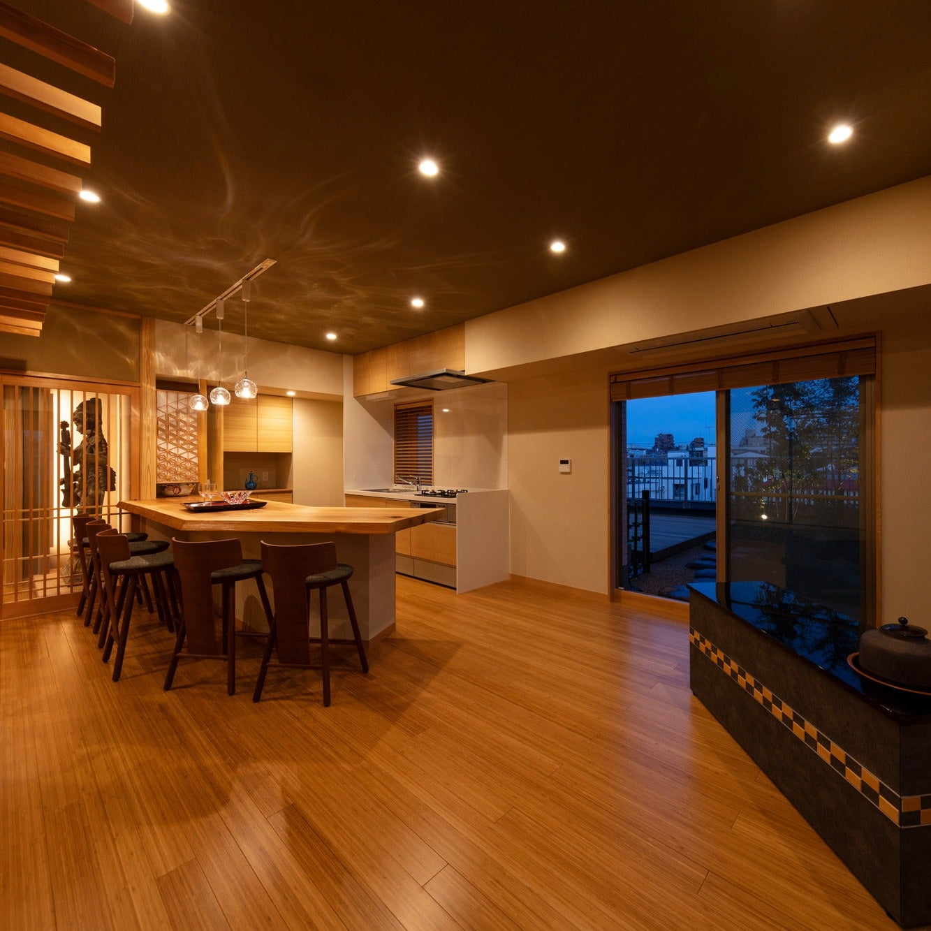 Open-plan top-floor salon at dusk with a timber counter, a low hearth cabinet and an illuminated entrance alcove, a modern Japanese interior in Tokyo.