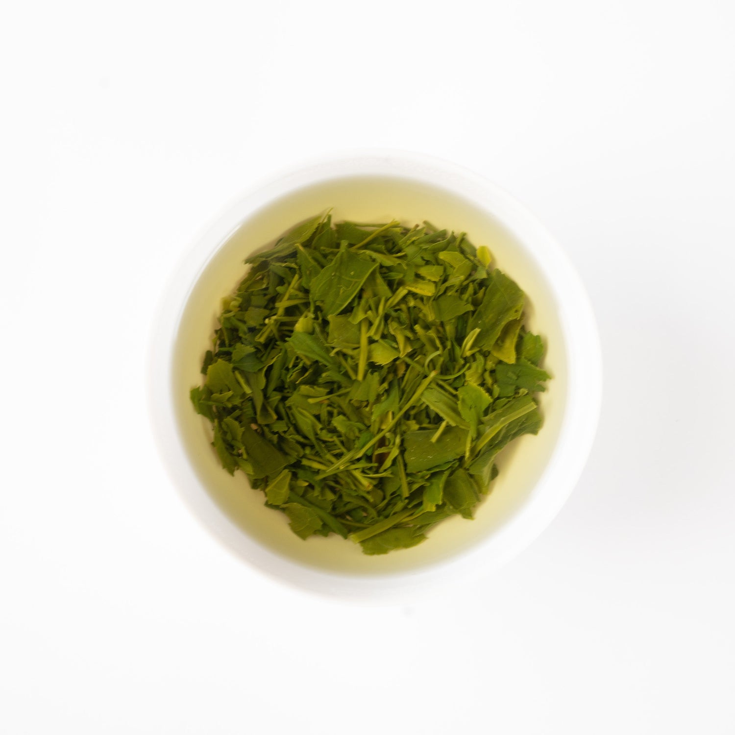 A top-down minimalist view of vibrant green Sencha tea leaves steeping beautifully inside a clean white ceramic cup.