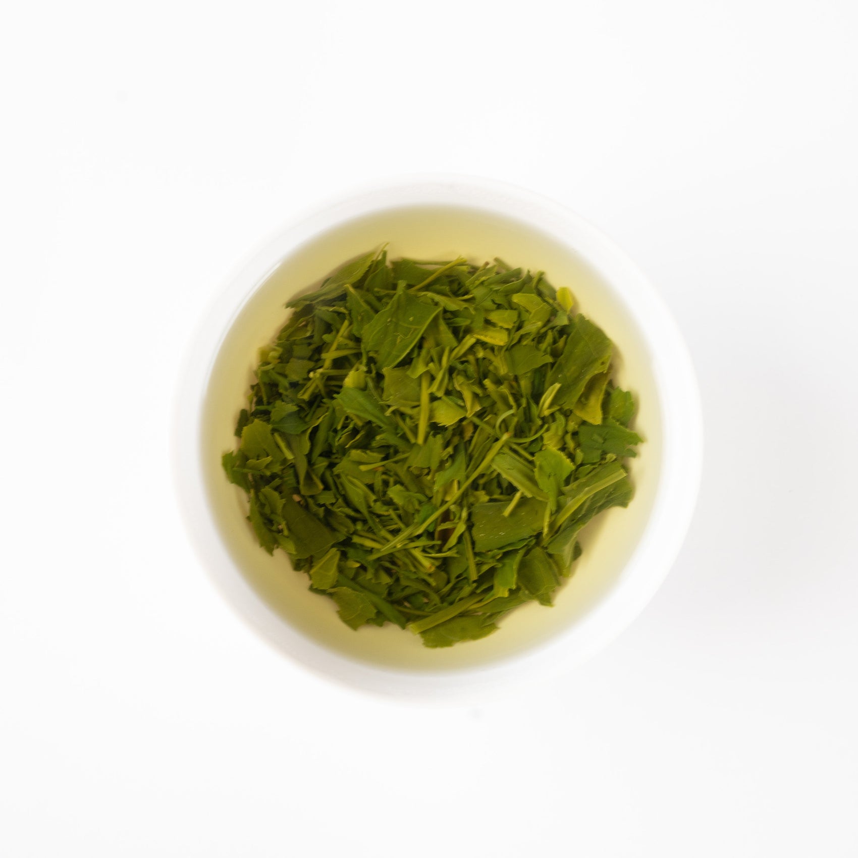 A top-down minimalist view of vibrant green Sencha tea leaves steeping beautifully inside a clean white ceramic cup.