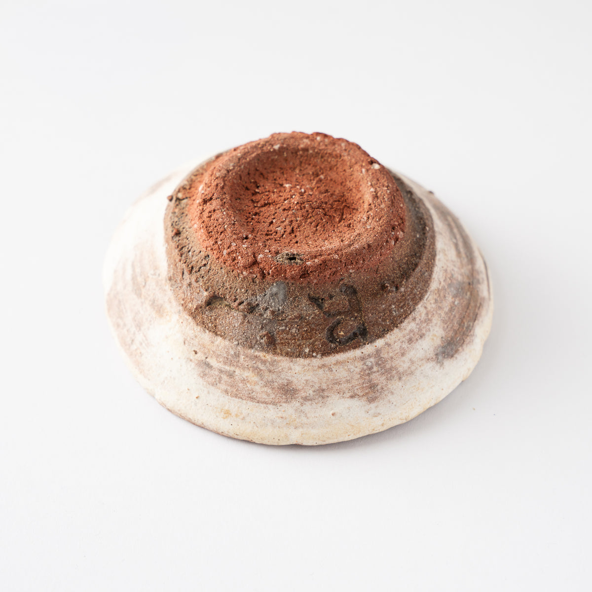 Inverted view showing the raw terracotta red-clay foot base of Ryusuke Asai's shallow ceramic GUINOMI sake cup.