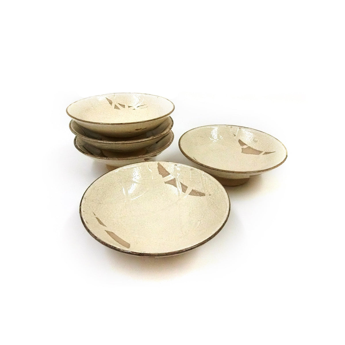 The five cream-glazed shallow bowls on a white ground, four stacked and one in front, the brown rims and bare-clay patches visible.