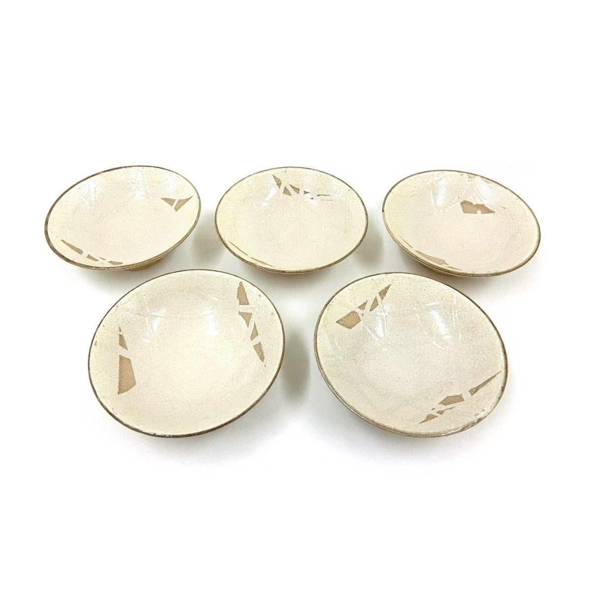 The five bowls laid out flat from above, each showing different angular unglazed patches in the crackled cream glaze.