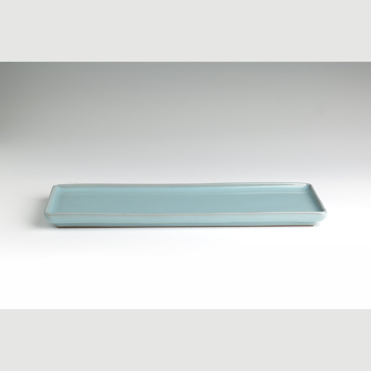 The pale blue-green celadon rectangular plate on a grey ground, viewed from the front at a low angle.