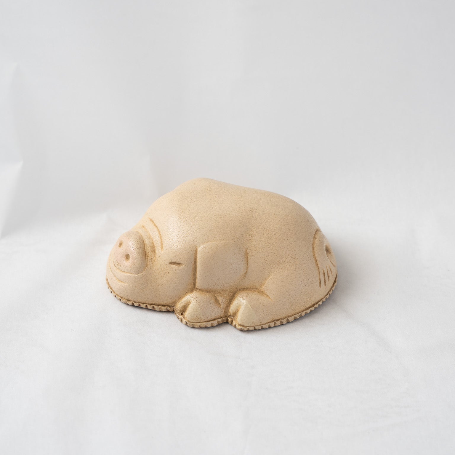 Left side profile of the resting leather pig sculpture, showcasing the plump, rounded body contour and clean transitions of the molded leather form.