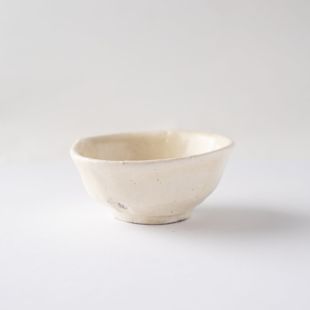 Turned profile view of Seiya Toyoba's creamy ivory Kohiki SAKAZUKI sake cup against a plain studio background.