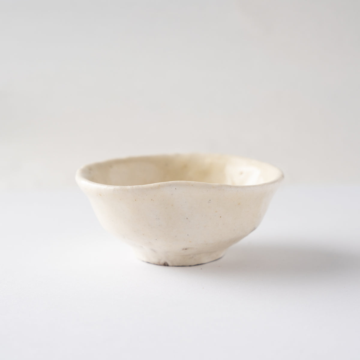Side view of Seiya Toyoba's Kohiki SAKAZUKI sake cup, showing a smooth creamy white glaze and gentle rim curve.