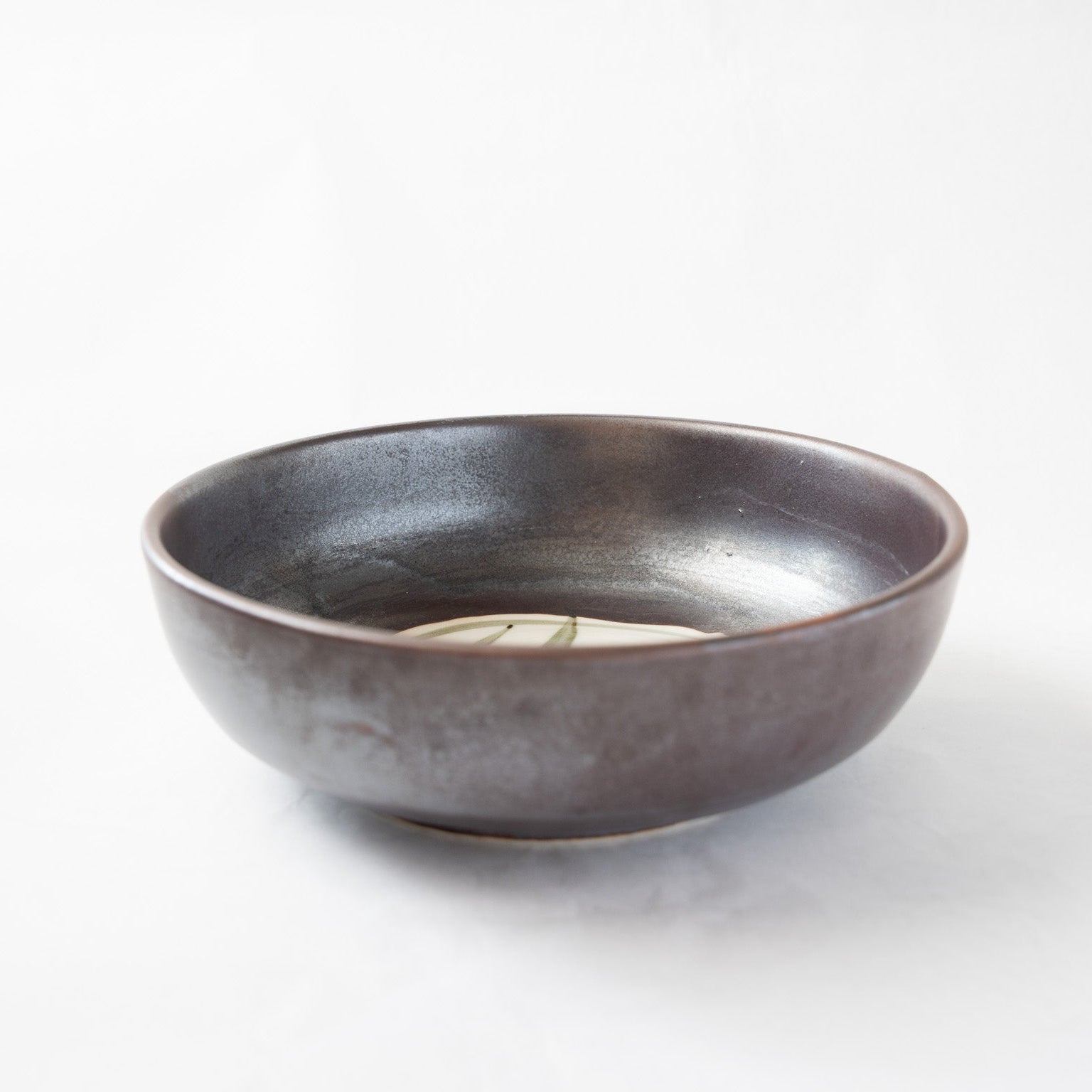 A detailed angled top-view of the Shigaraki iron-glazed confectionery bowl by Katsuhiko Sato, showcasing its dark, metallic-sheen profile and a glimpse of the internal white slip patch with its minimalist linear drawing.