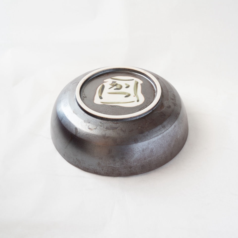 Detail view of the base of the iron-glazed Shigaraki bowl, highlighting the dark metallic glaze texture and the hand-painted artist signature inside the foot.