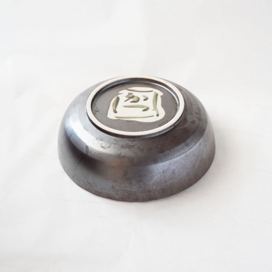 Detail view of the base of the iron-glazed Shigaraki bowl, highlighting the dark metallic glaze texture and the hand-painted artist signature inside the foot.