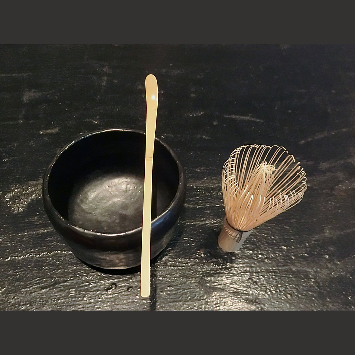 The tea bowl set on a dark surface with a bamboo tea scoop and whisk, whisked tea inside.