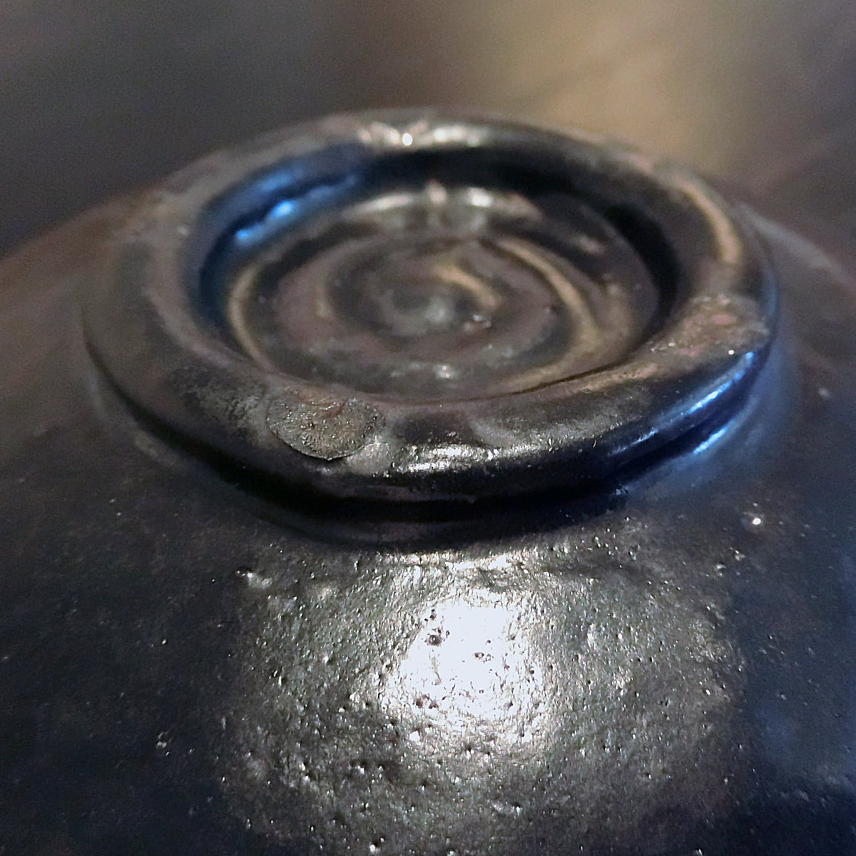 Close detail of the foot ring under the black glaze, a spiral trimming trace and a bluish sheen in raking light.