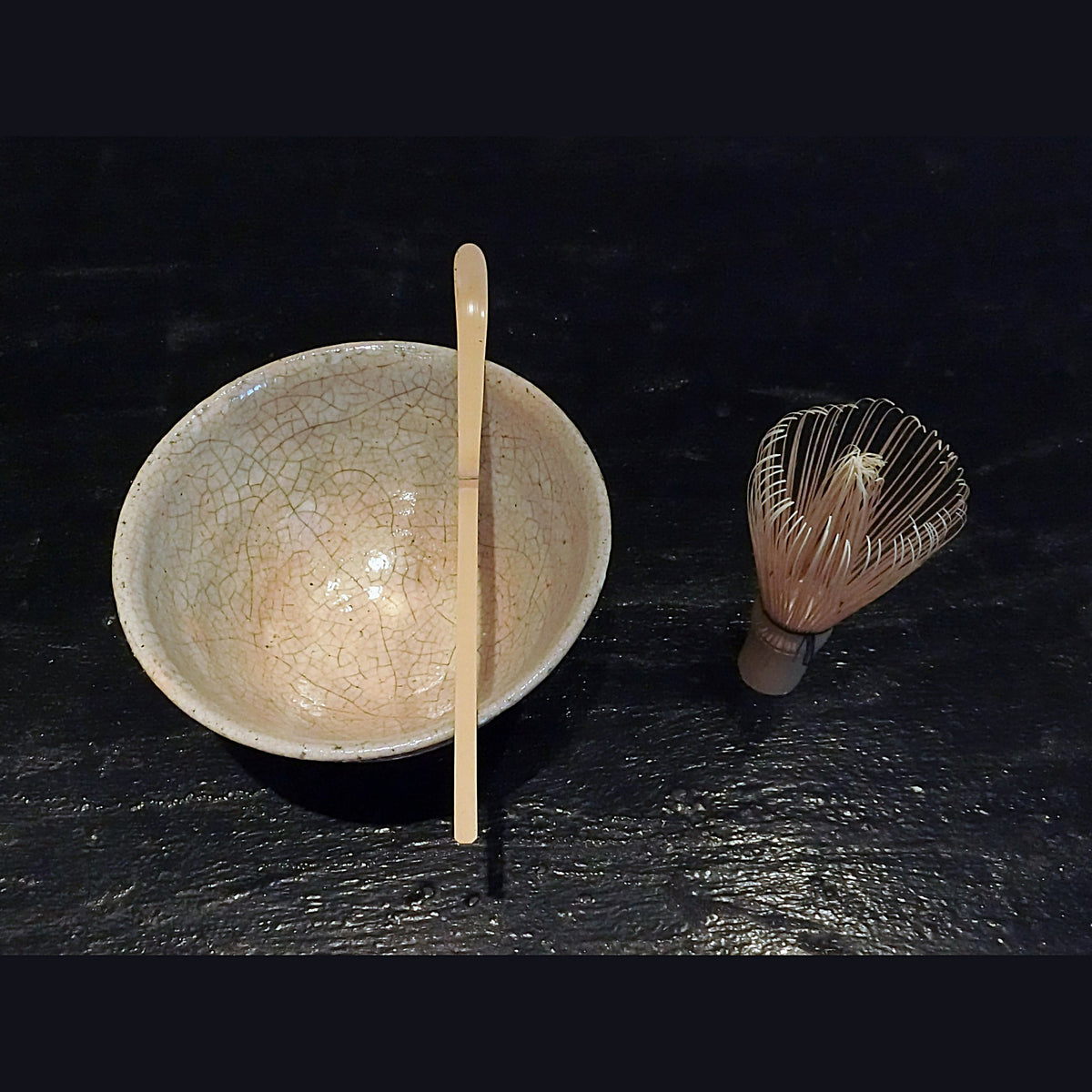 Le bol sur une surface sombre, accompagné d'une cuillère et d'un fouet en bambou, le thé battu à l'intérieur.