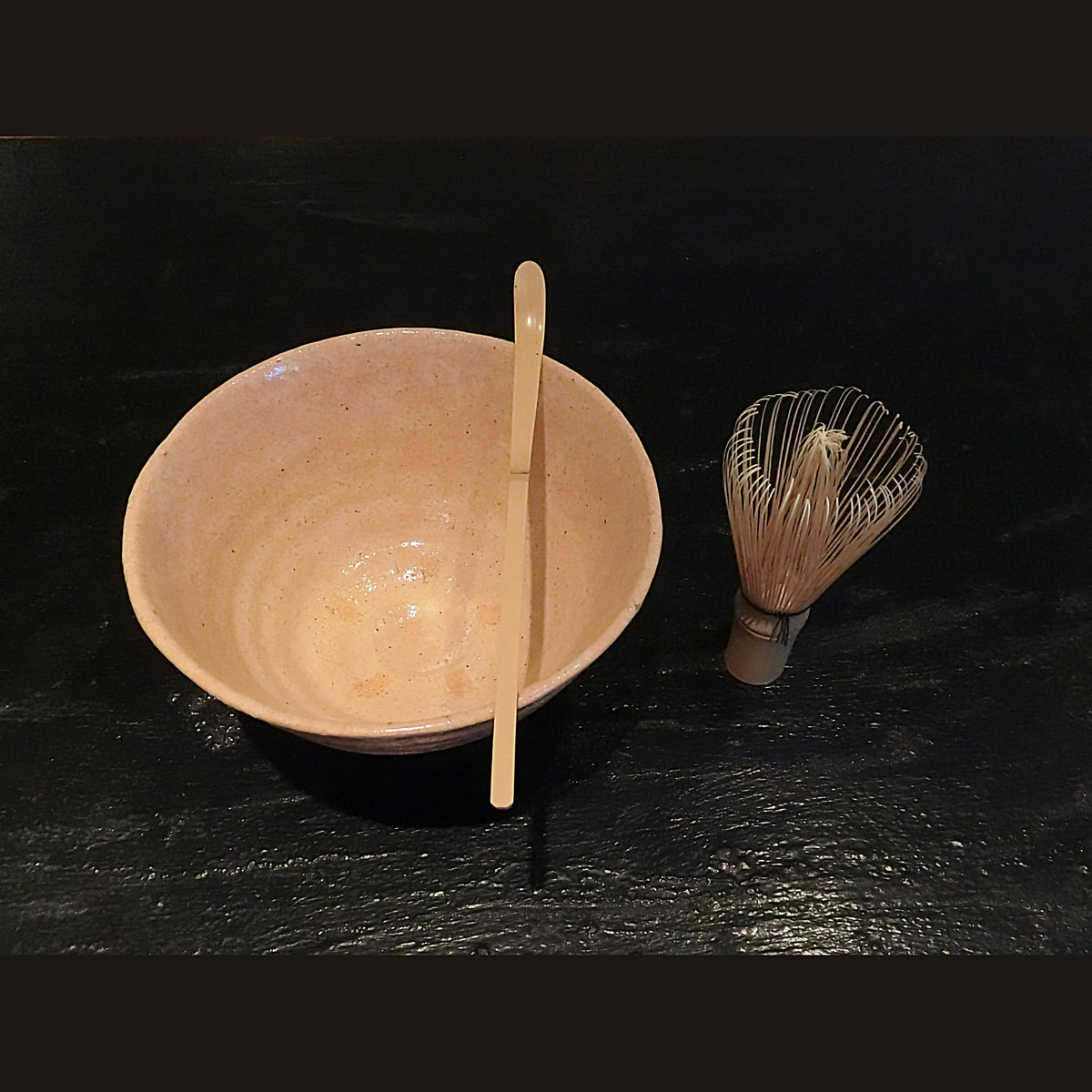 暗い面の上に、竹の茶杓と茶筅とともに置かれた茶盌。茶が点てられている。