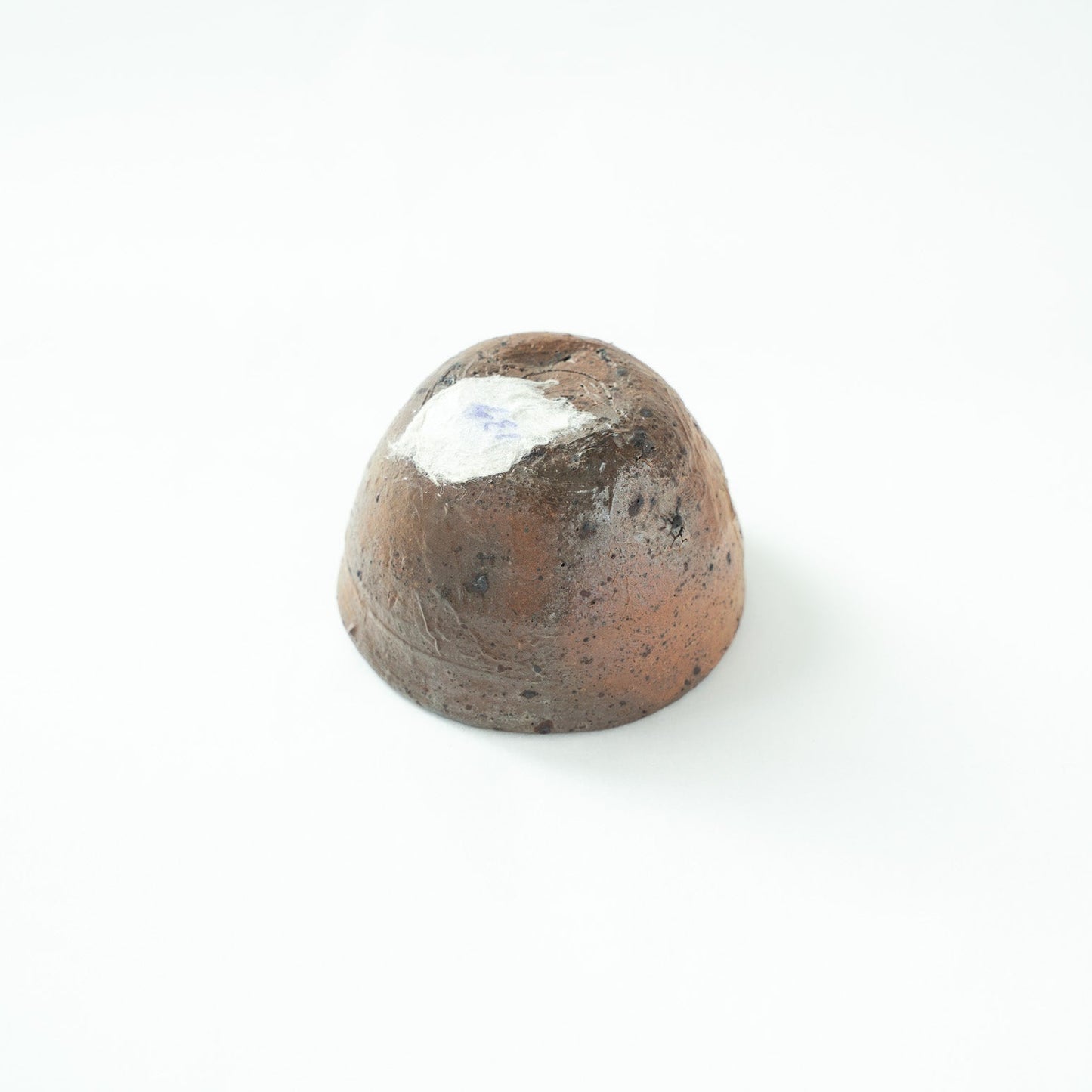 Inverted view of the GUINOMI, showing the raw, unpolished bottom surface with a white collection sticker attached to the base.