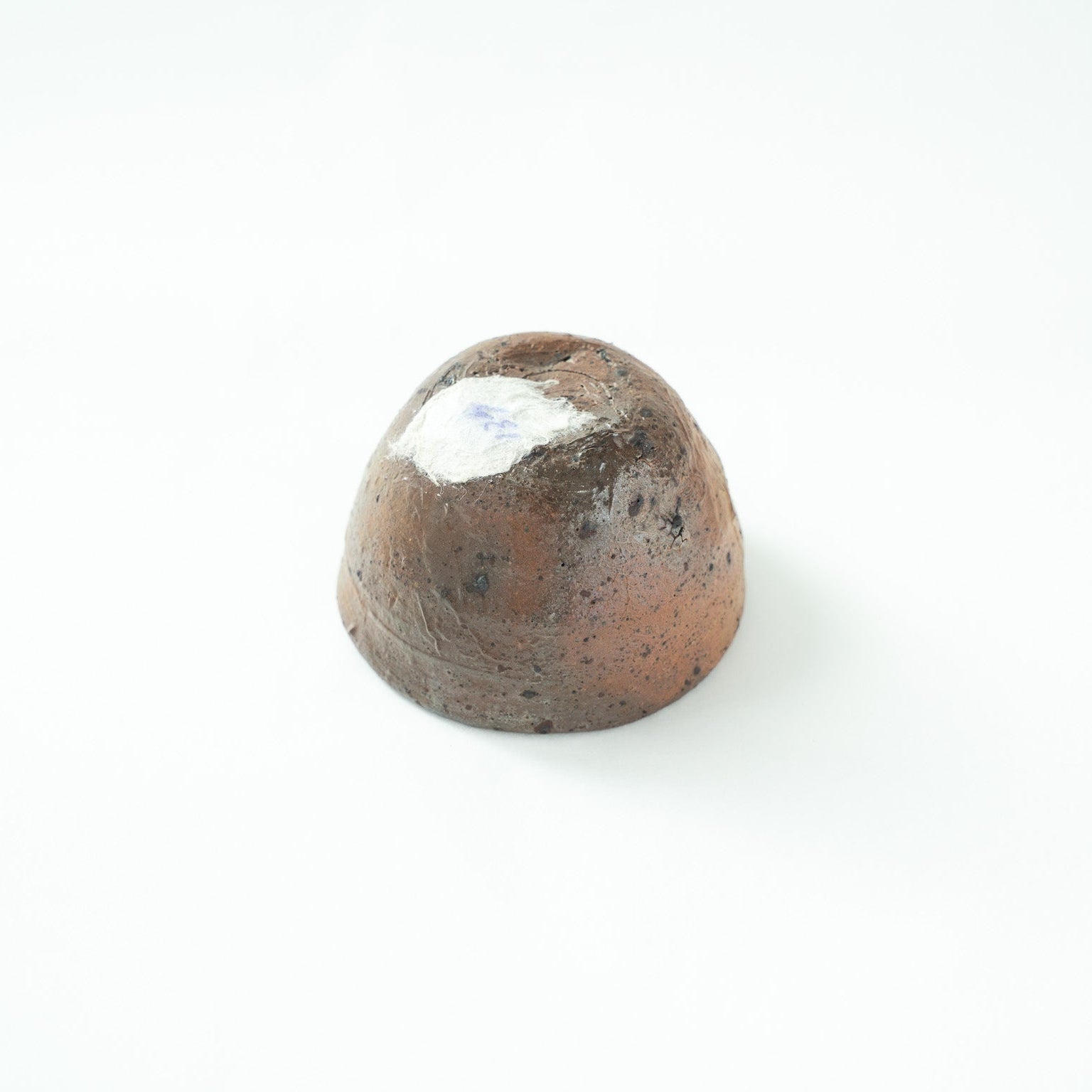 Inverted view of the GUINOMI, showing the raw, unpolished bottom surface with a white collection sticker attached to the base.