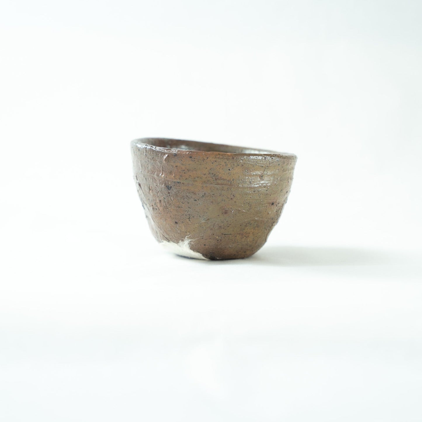 Alternate profile shot of the unrefined ceramic cup, revealing its organic silhouette and a partial view of the white sticker on the base.