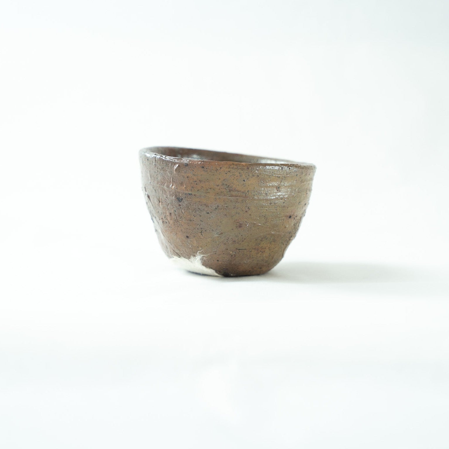 Alternate profile shot of the unrefined ceramic cup, revealing its organic silhouette and a partial view of the white sticker on the base.