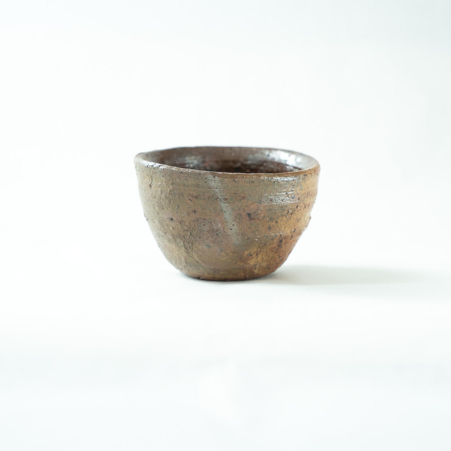 Side view of Shiro Tsujimura's sake cup, highlighting the spontaneous firing marks and natural ash glaze reflections on the rustic surface.