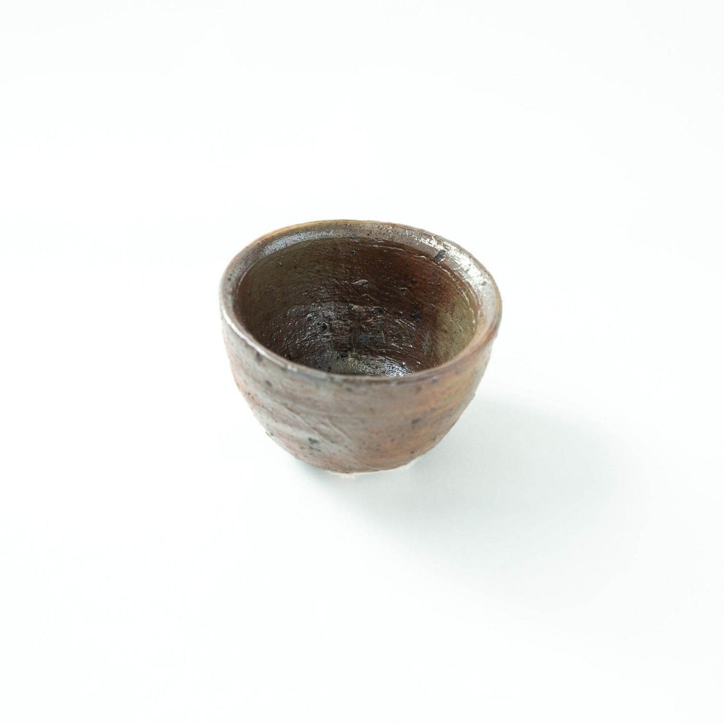 Top-down angled view looking inside the deep, unpolished interior of the ceramic sake cup, showcasing the rich, dark textures within.