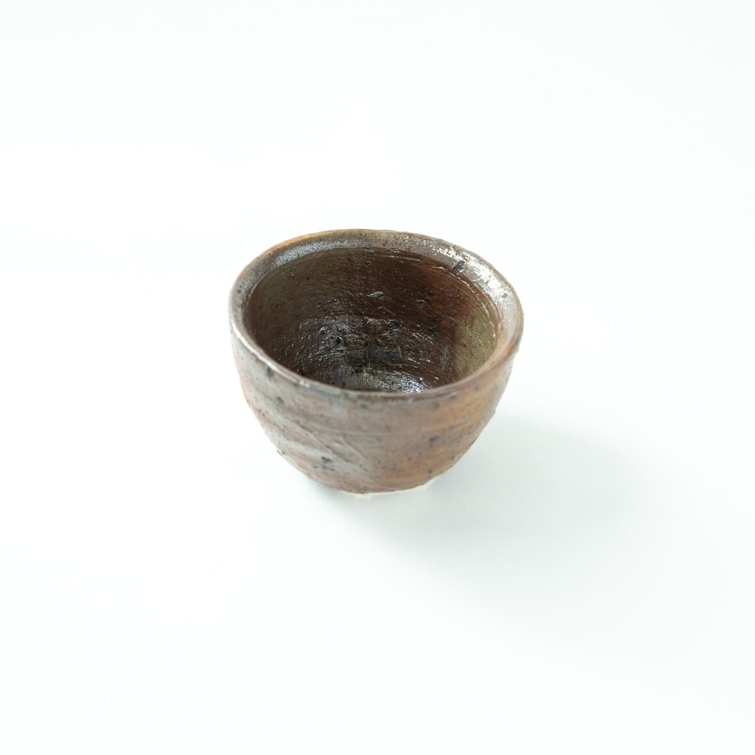 Top-down angled view looking inside the deep, unpolished interior of the ceramic sake cup, showcasing the rich, dark textures within.