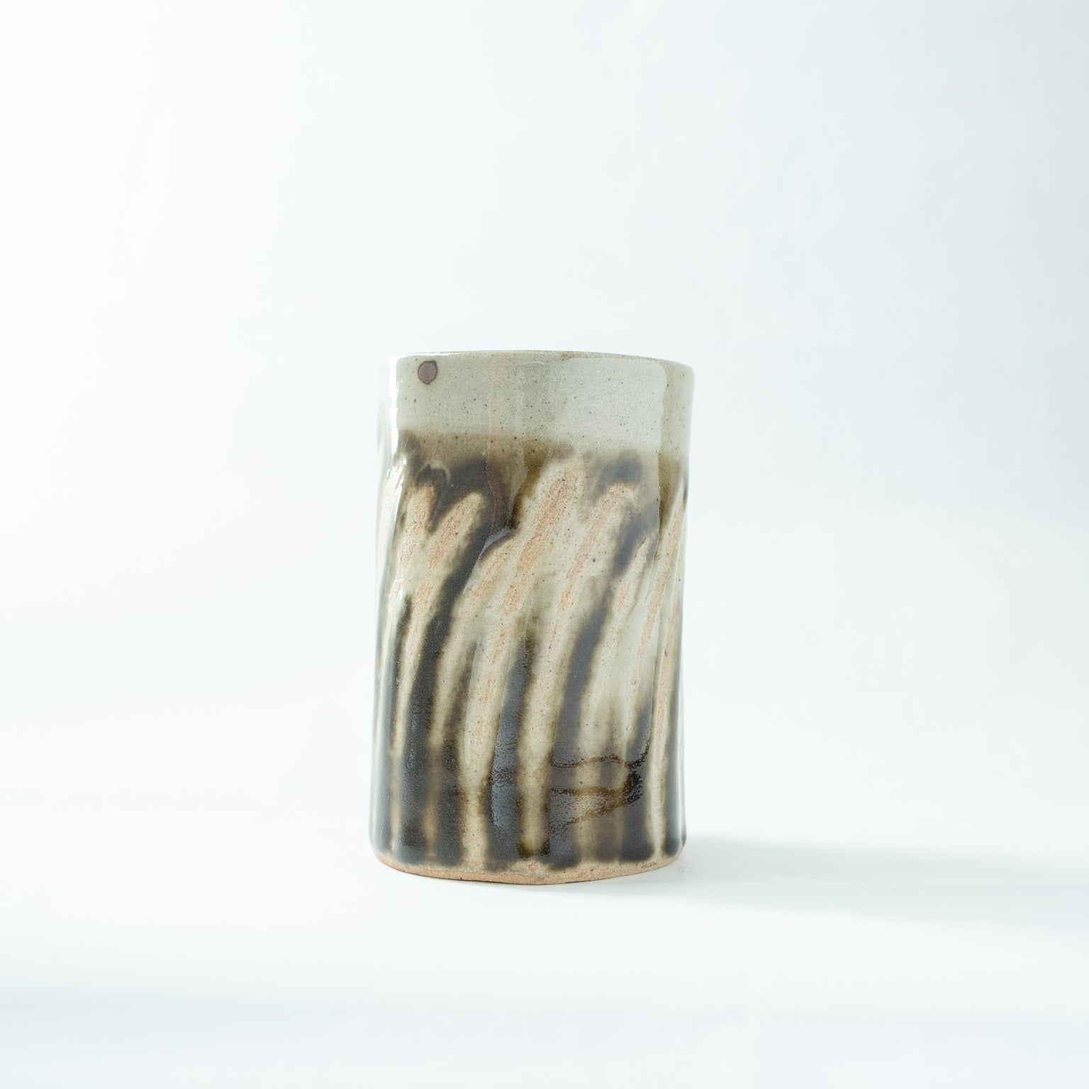 Front view of the cylindrical Mashiko ware HANAIRE by Shoji Hamada, showing the bold resist-wiped striped patterns over a dark iron glaze.