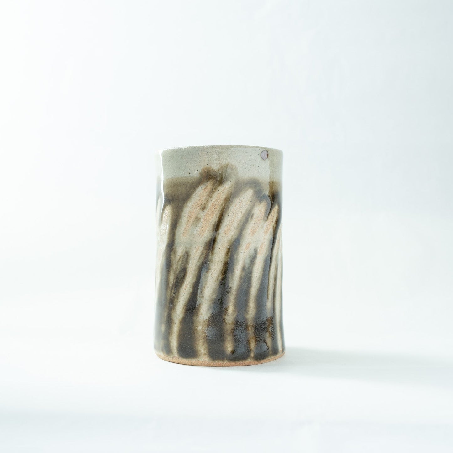 Side view of the Shoji Hamada cylindrical vase, highlighting the textured contrast between the cream-colored rim and the fluid dark glaze stripes.