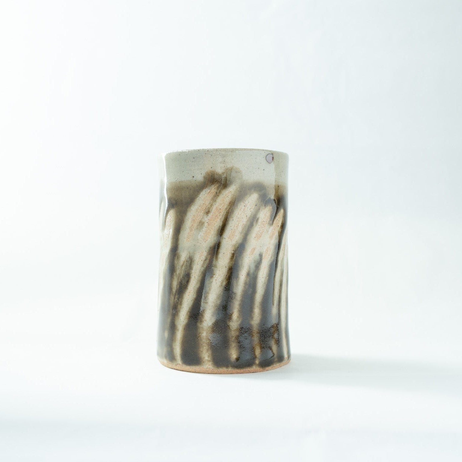 Side view of the Shoji Hamada cylindrical vase, highlighting the textured contrast between the cream-colored rim and the fluid dark glaze stripes.