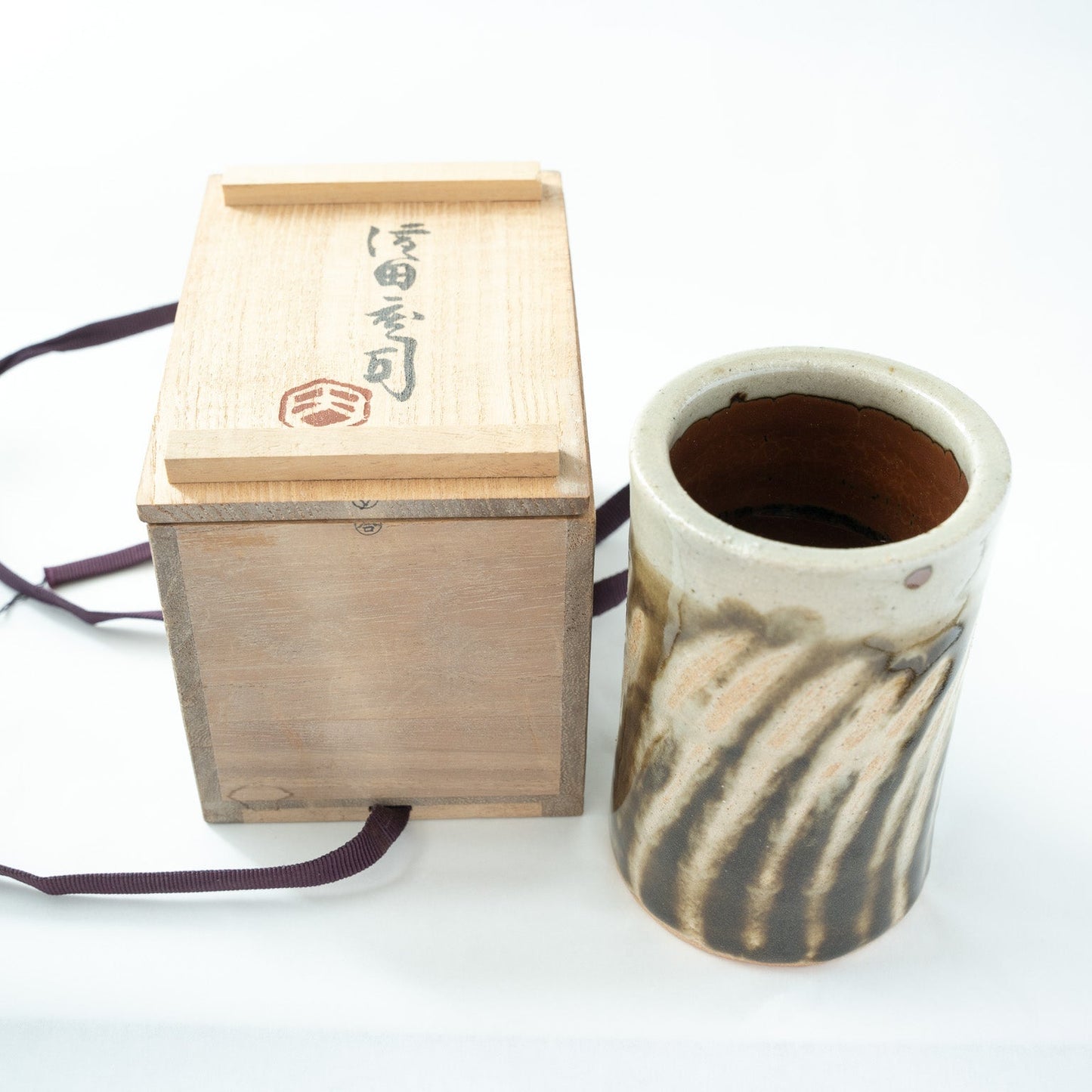 The Shoji Hamada cylindrical flower vase shown next to its original signed wooden box featuring the artist's calligraphy and red stamp.