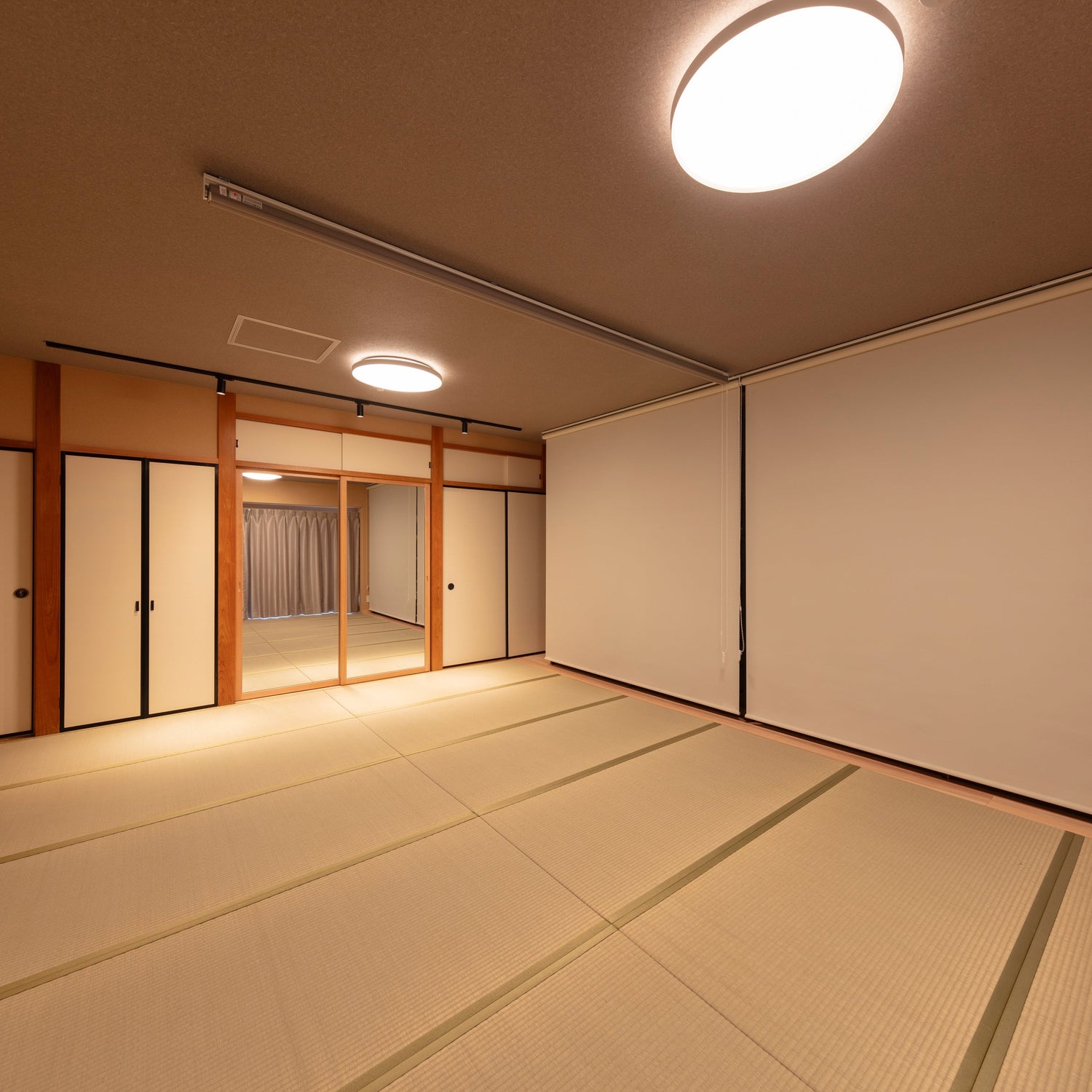 A spacious modern Japanese-style room featuring tatami mat flooring, fusuma sliding doors, and soft ambient lighting.