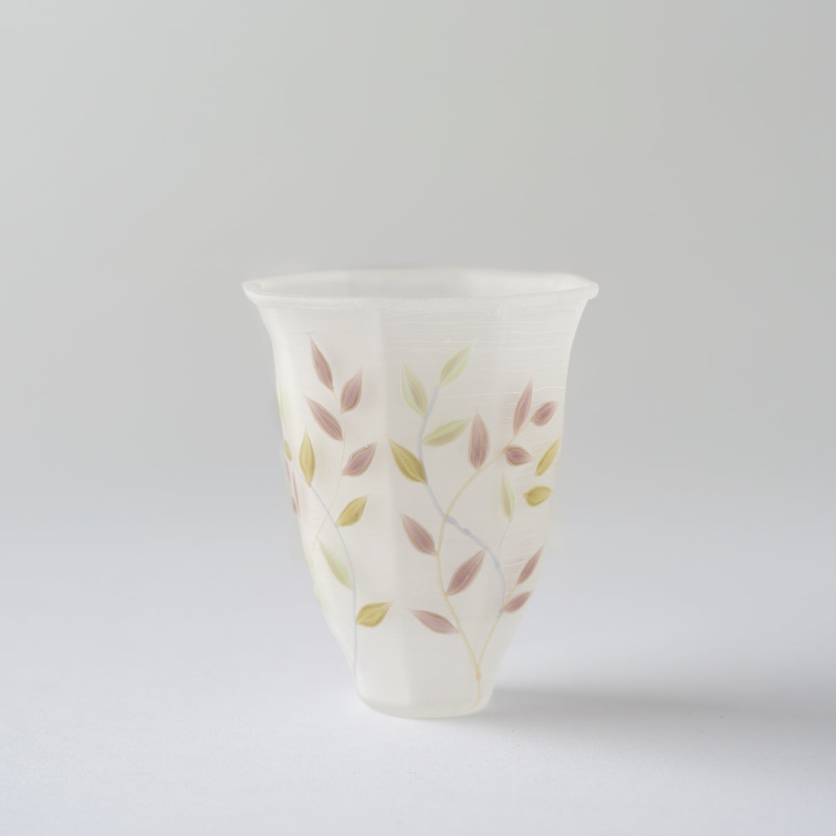 Studio view of the octagonal white glass GUINOMI cup by Toru Sato, displaying the delicate vine pattern against a neutral background.