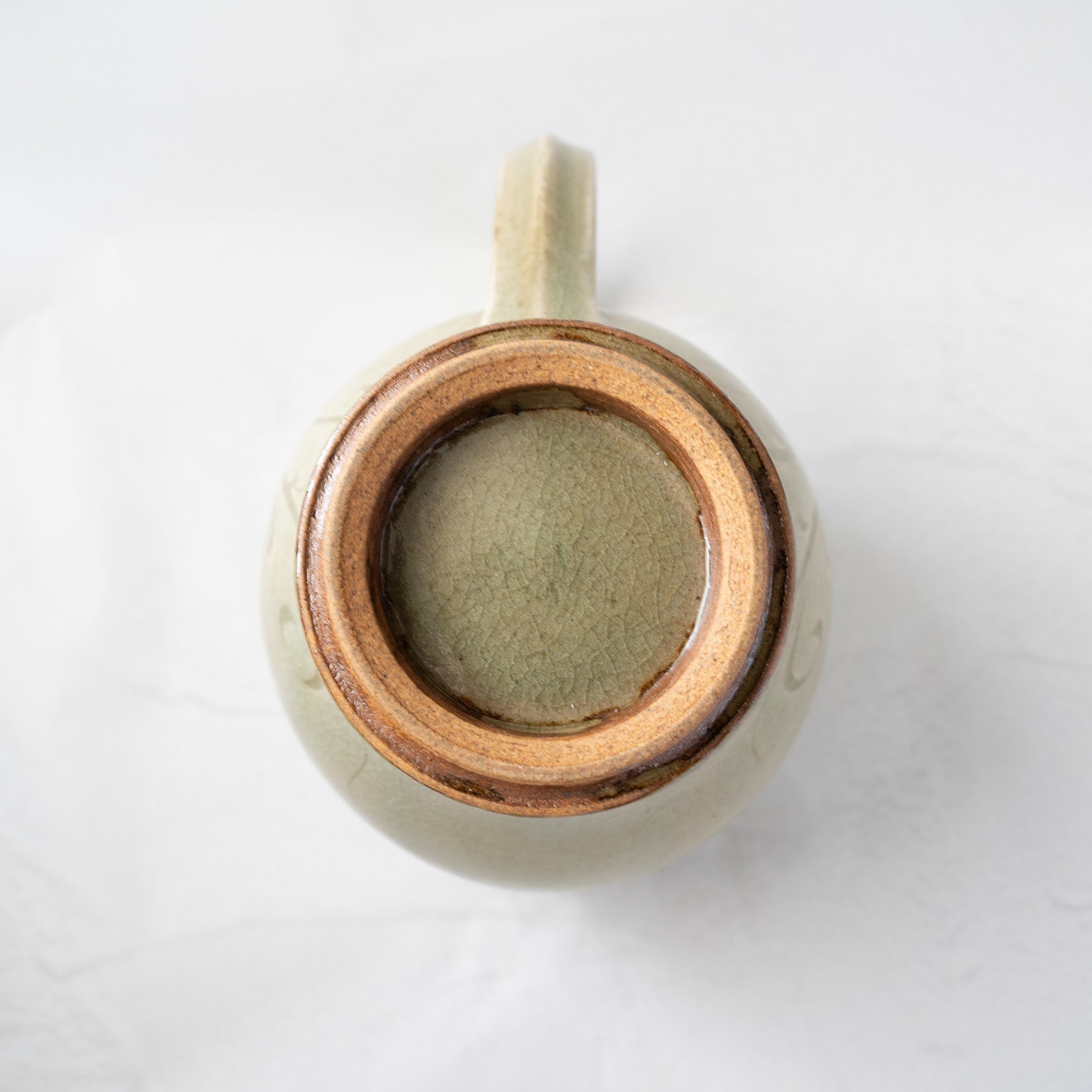 Direct view of the underside of the pitcher, showing the circular, unglazed reddish-brown clay foot ring contrasting with the crackle-glazed base interior.