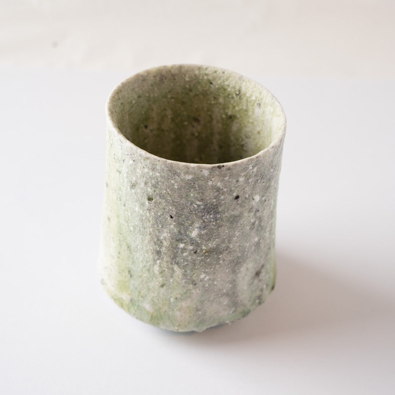 High-angle view of a cylinder-shaped natural glaze YUNOMI cup by Yui Tsujimura, showing a pale green vidro glaze cascade and rough ash-textured surface.