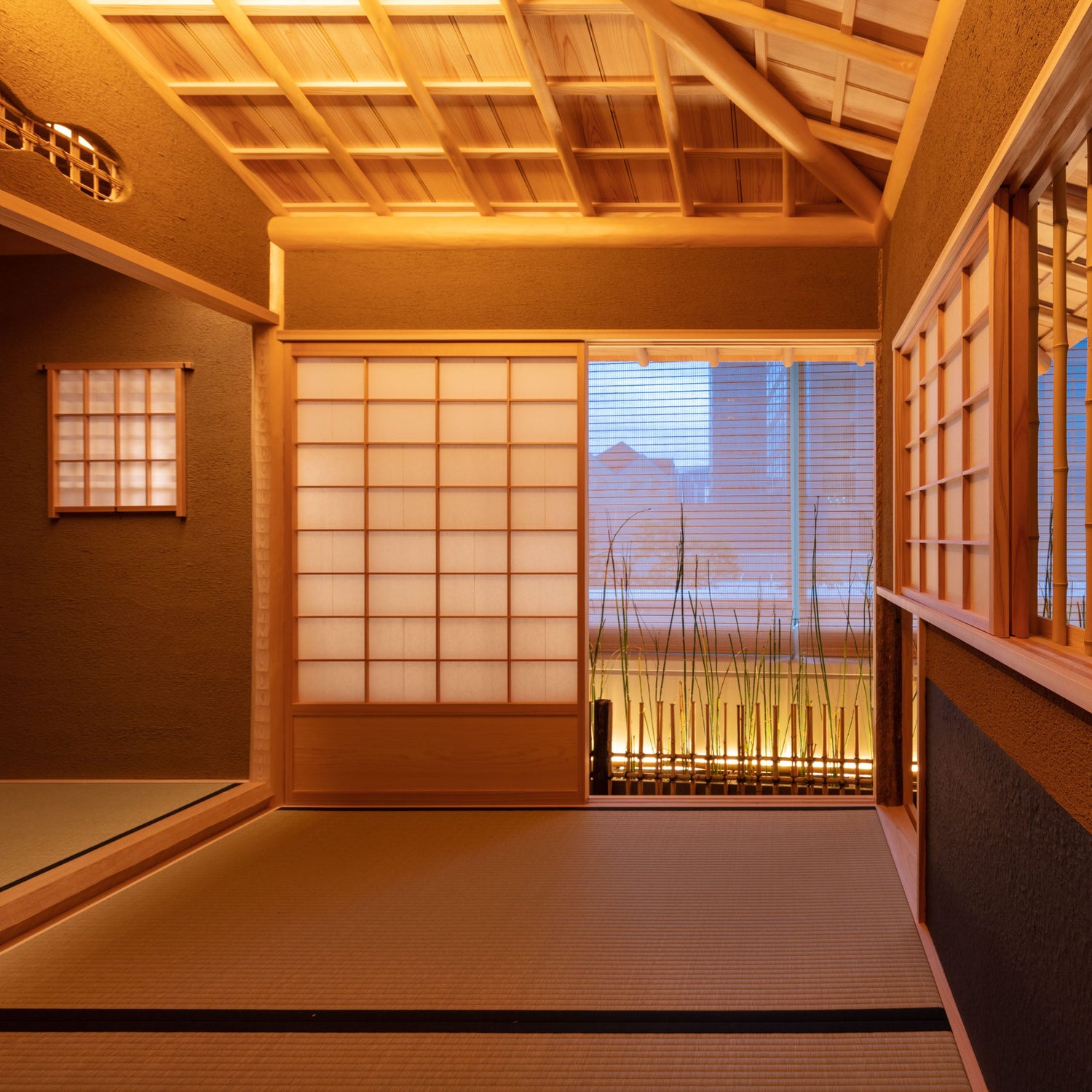 Intérieur de salle de thé : murs de terre sombres et texturés, tatami, plafond de bois à caissons, et des shoji ouvrant sur des bambous éclairés.