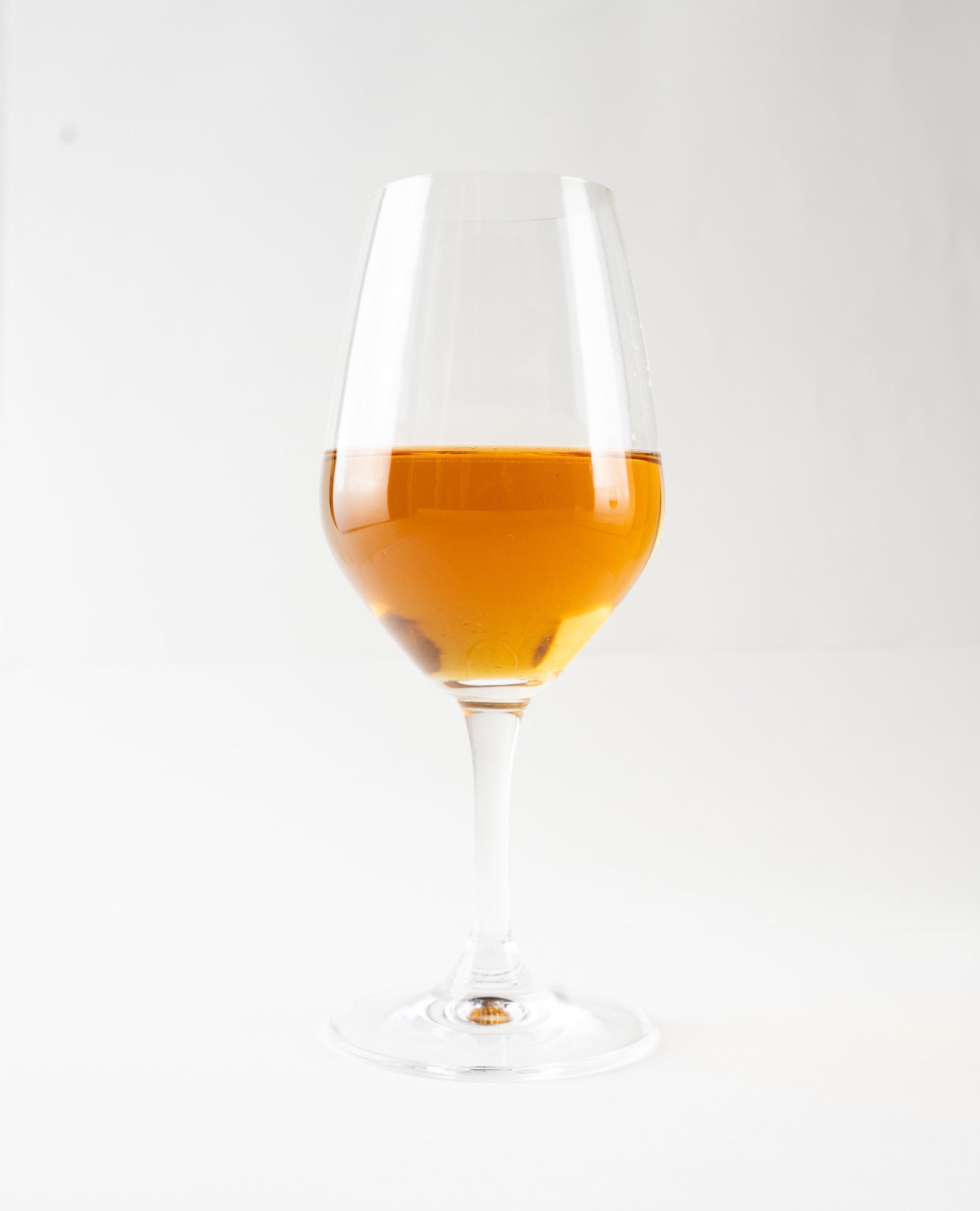 Clear amber hojicha tea served in an elegant wine glass, capturing the warm light and pure liquid.