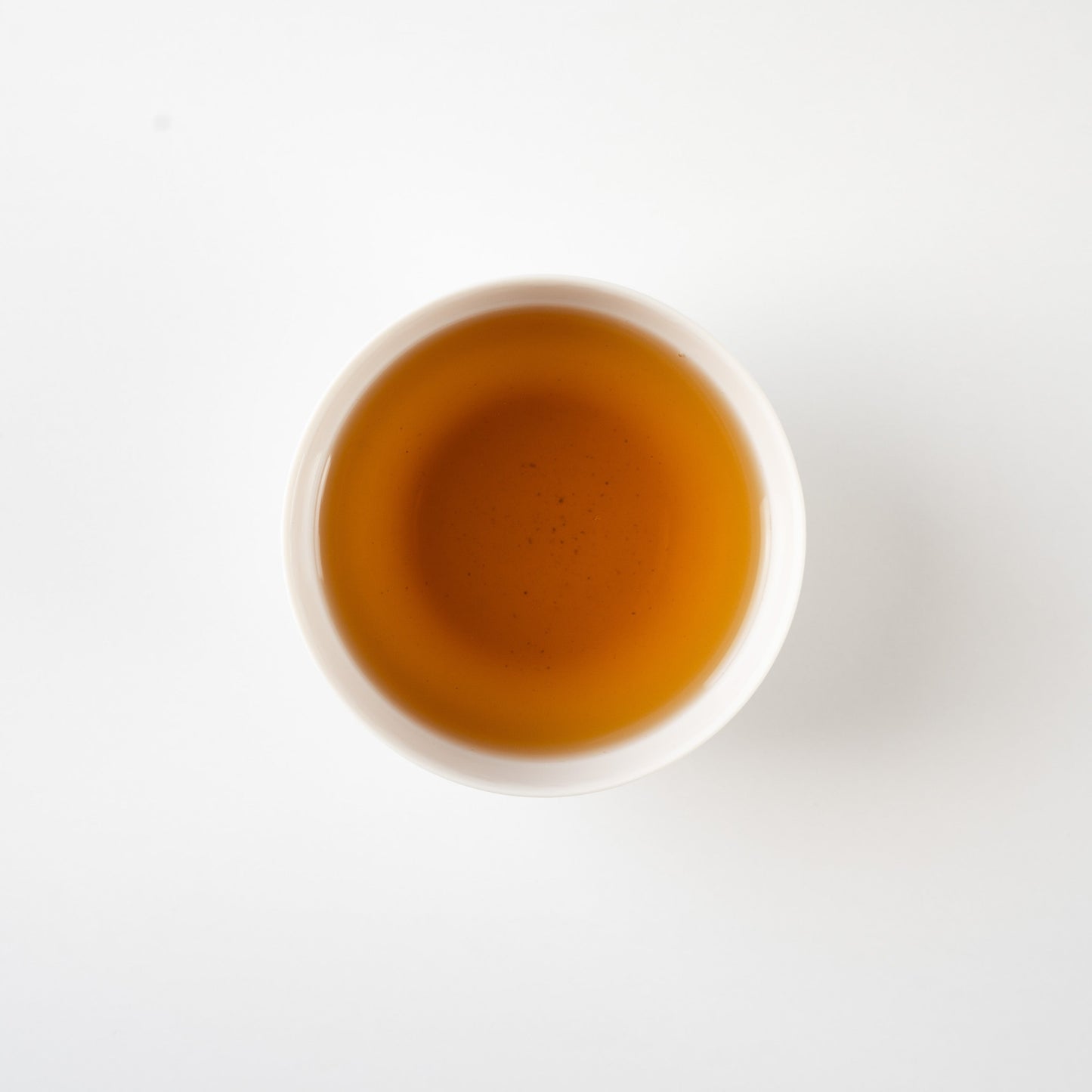 Top-down view of clear hojicha in a white teacup, revealing a gentle gradient of roasted amber tones.